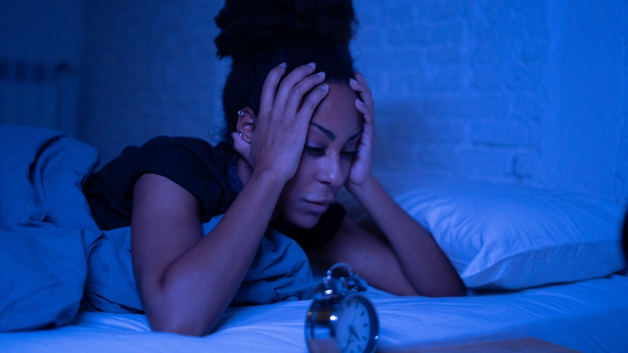 Image of a woman struggling to sleep with an alarm clock in the foreground