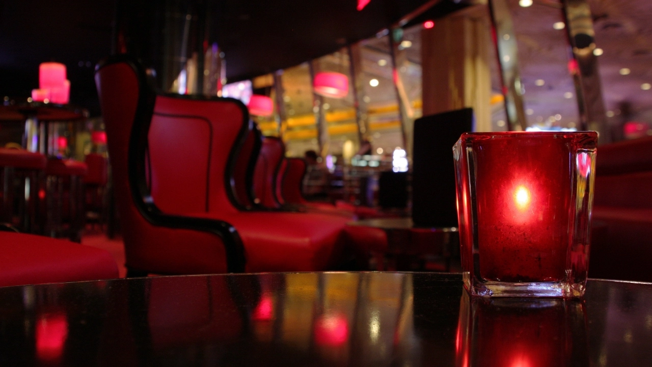 Image of a darkly lit lounge wit a red candle sitting on a table in the foreground.