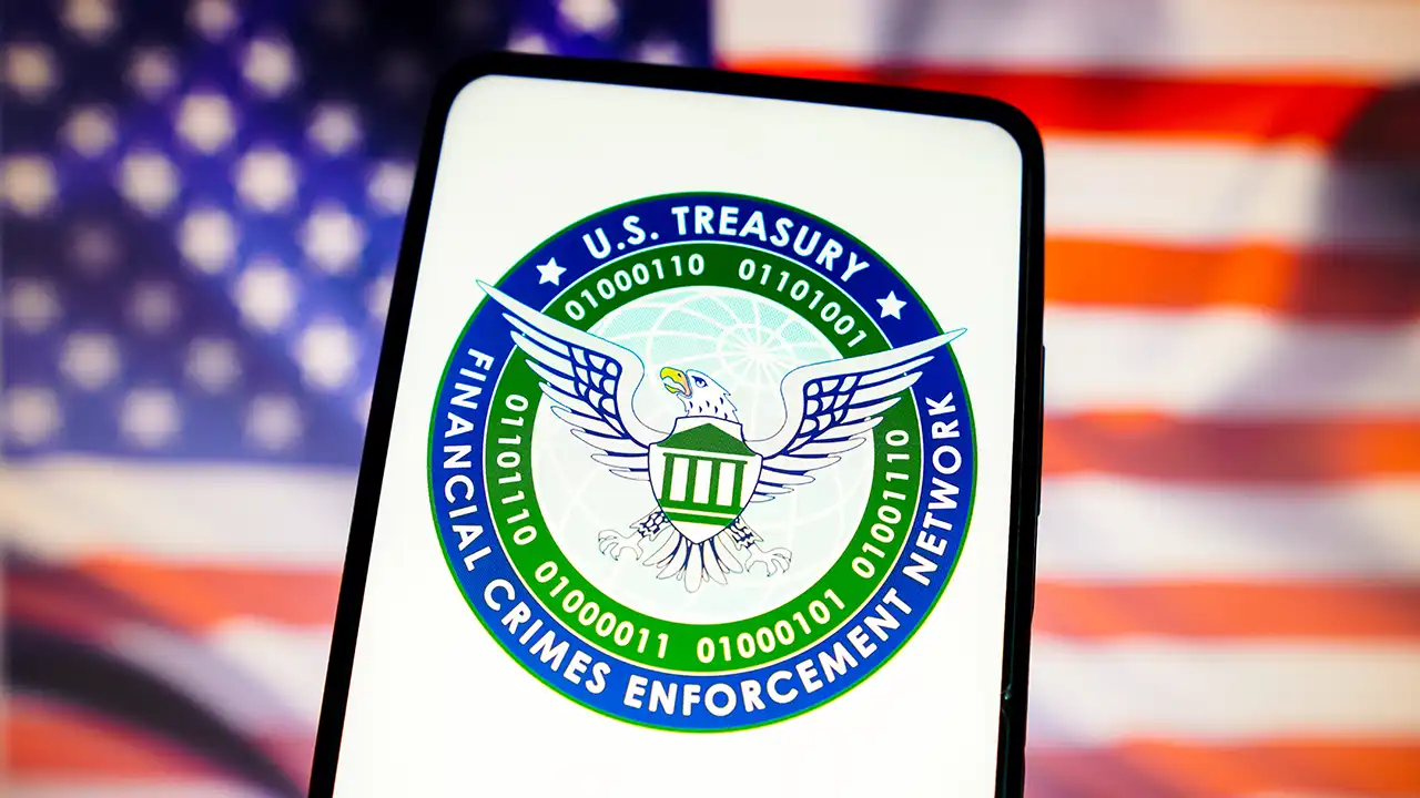 Image of U.S. Treasury’s Financial Crimes Enforcement Network (FinCEN) logo on a cellphone with U.S. flag in background