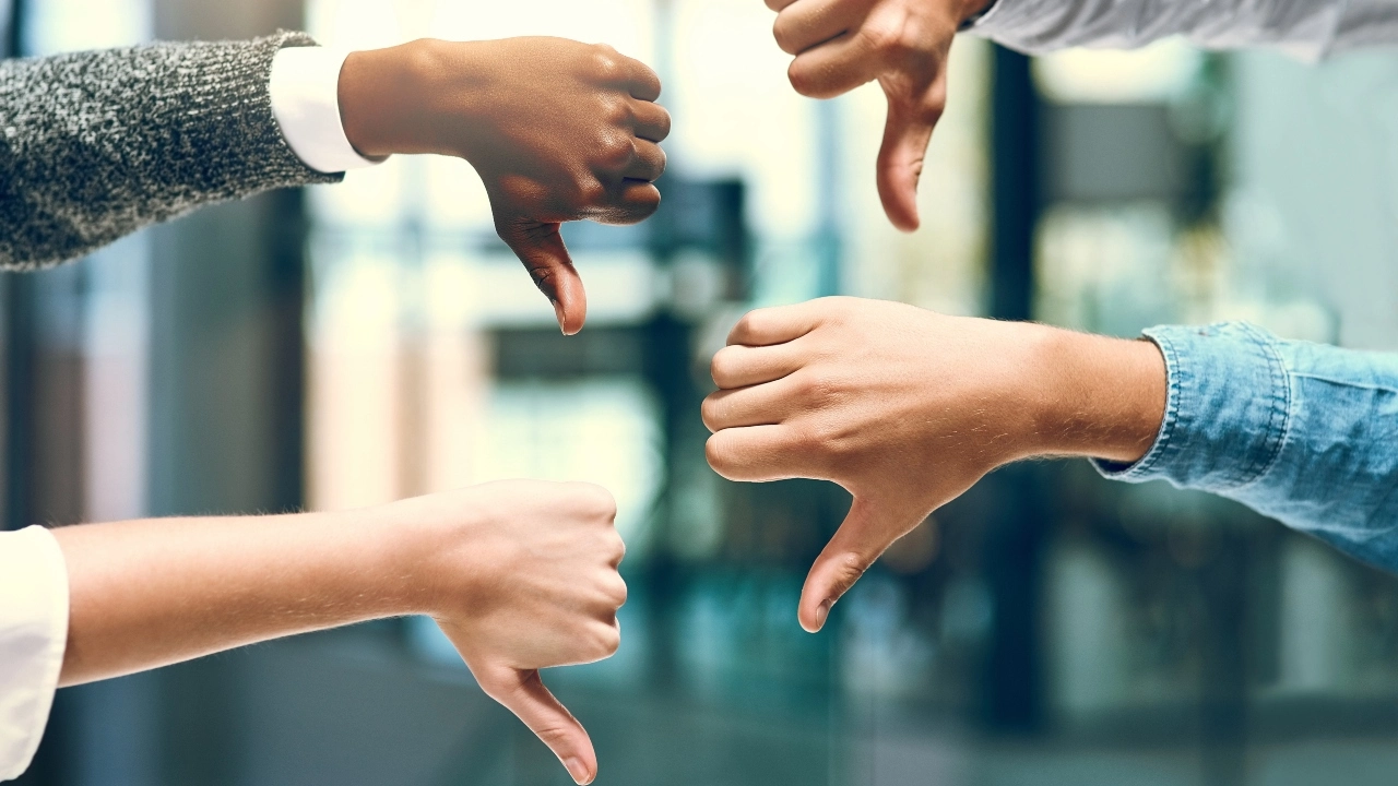 Image of four diverse people's hands giving the thumbs-down sign with their hands
